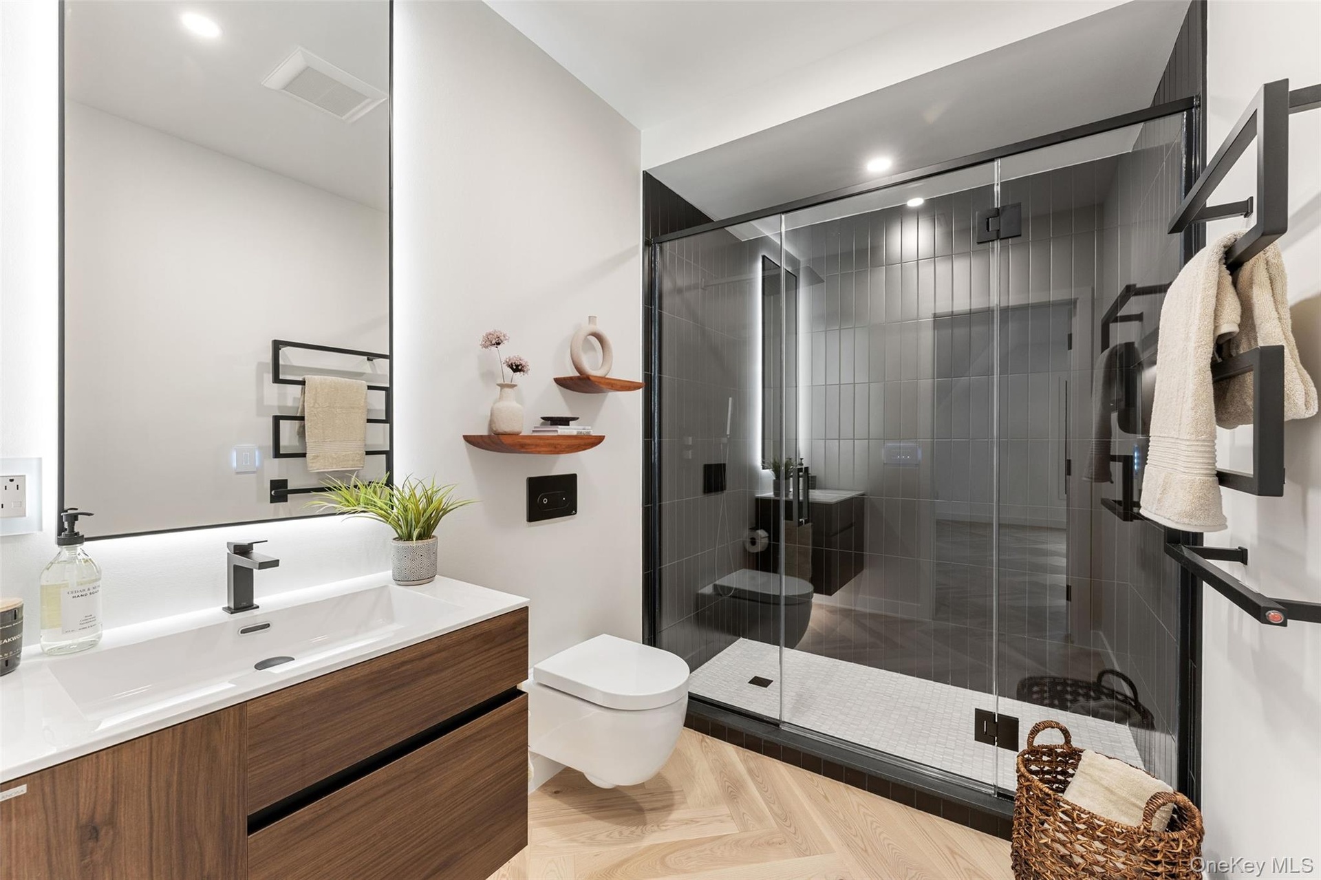 Modern ensuite bathroom in 2nd bedroom featuring a wood vanity with a white countertop, a rectangular mirror with backlighting, a glass-enclosed showe