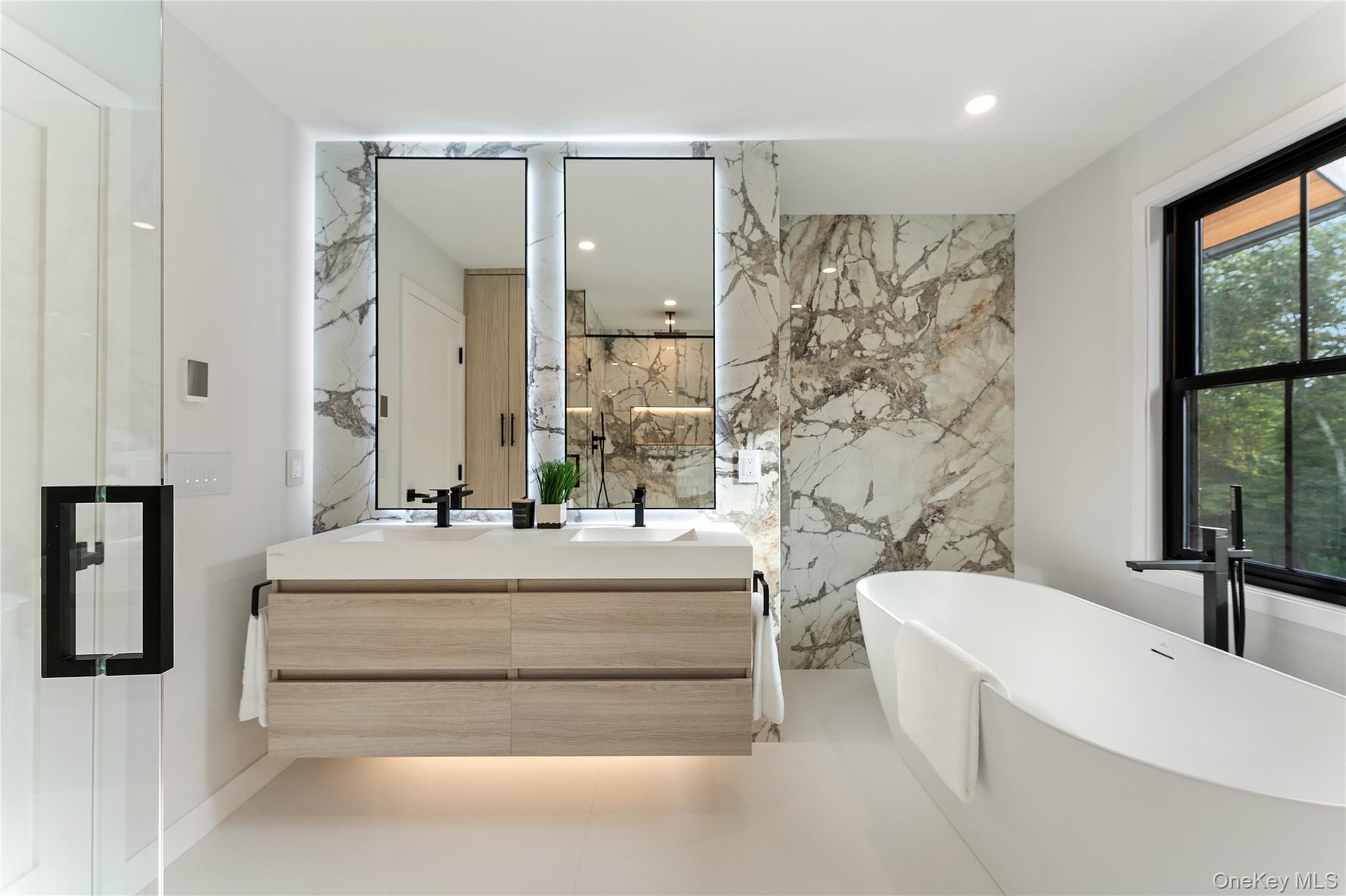 Full bathroom featuring double vanity, a freestanding bath, stone wall, and recessed lighting