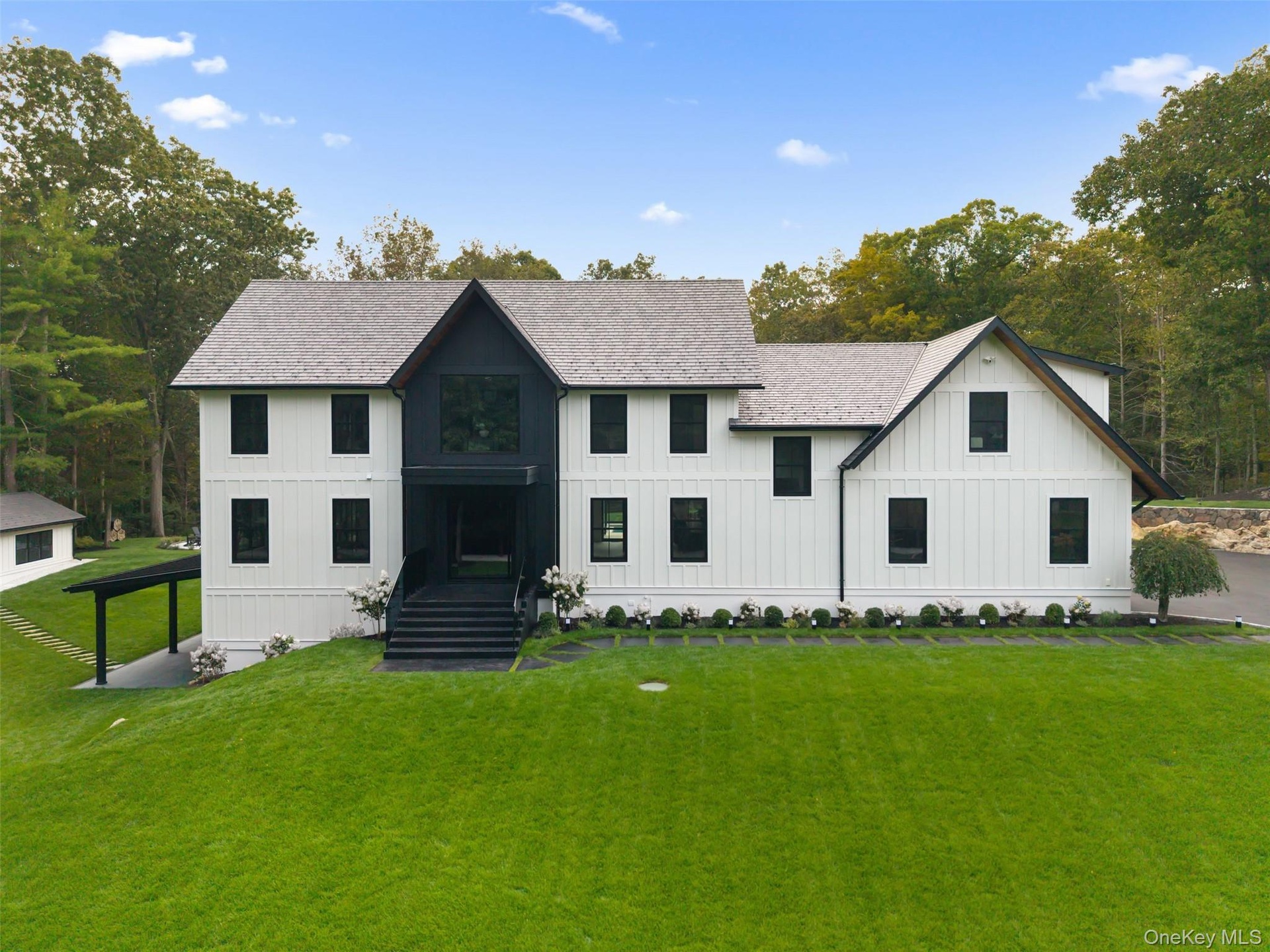 Modern inspired farmhouse with board and batten siding, a front yard, a shingled roof, and view of wooded area