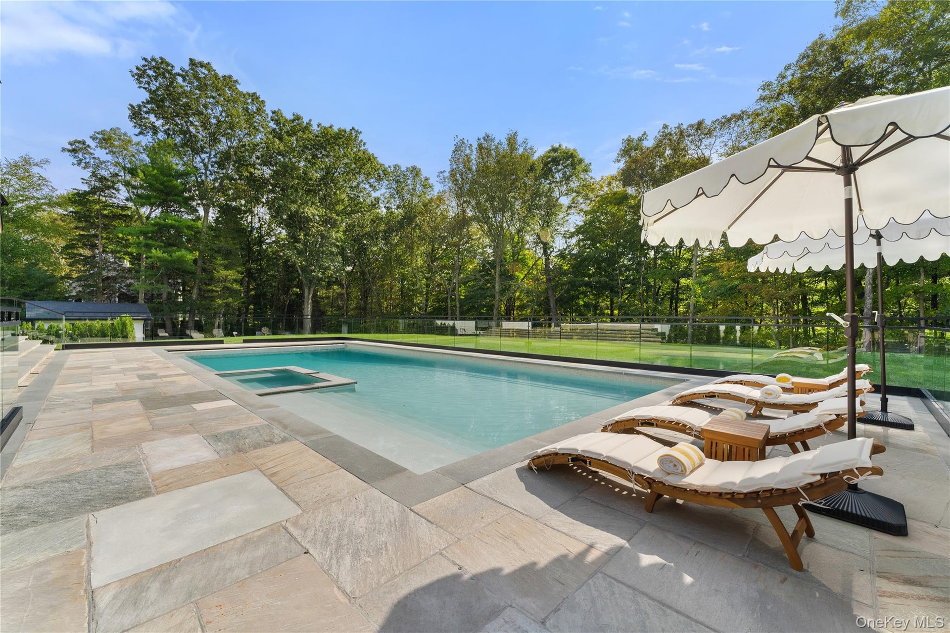 View of swimming pool featuring a patio, a pool with connected hot tub, and view of scattered trees