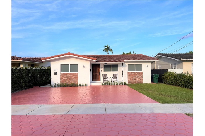 A well-maintained single-story duplex (units 3825 & 3827) with a Spanish-style tile roof, white stucco and brick accent facade, wood front door, and a
