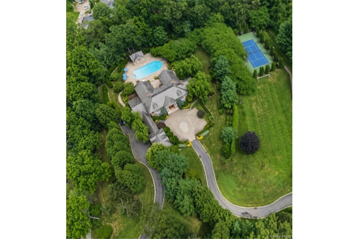 Expansive estate featuring a large swimming pool, paved patio areas, and a full-size tennis court