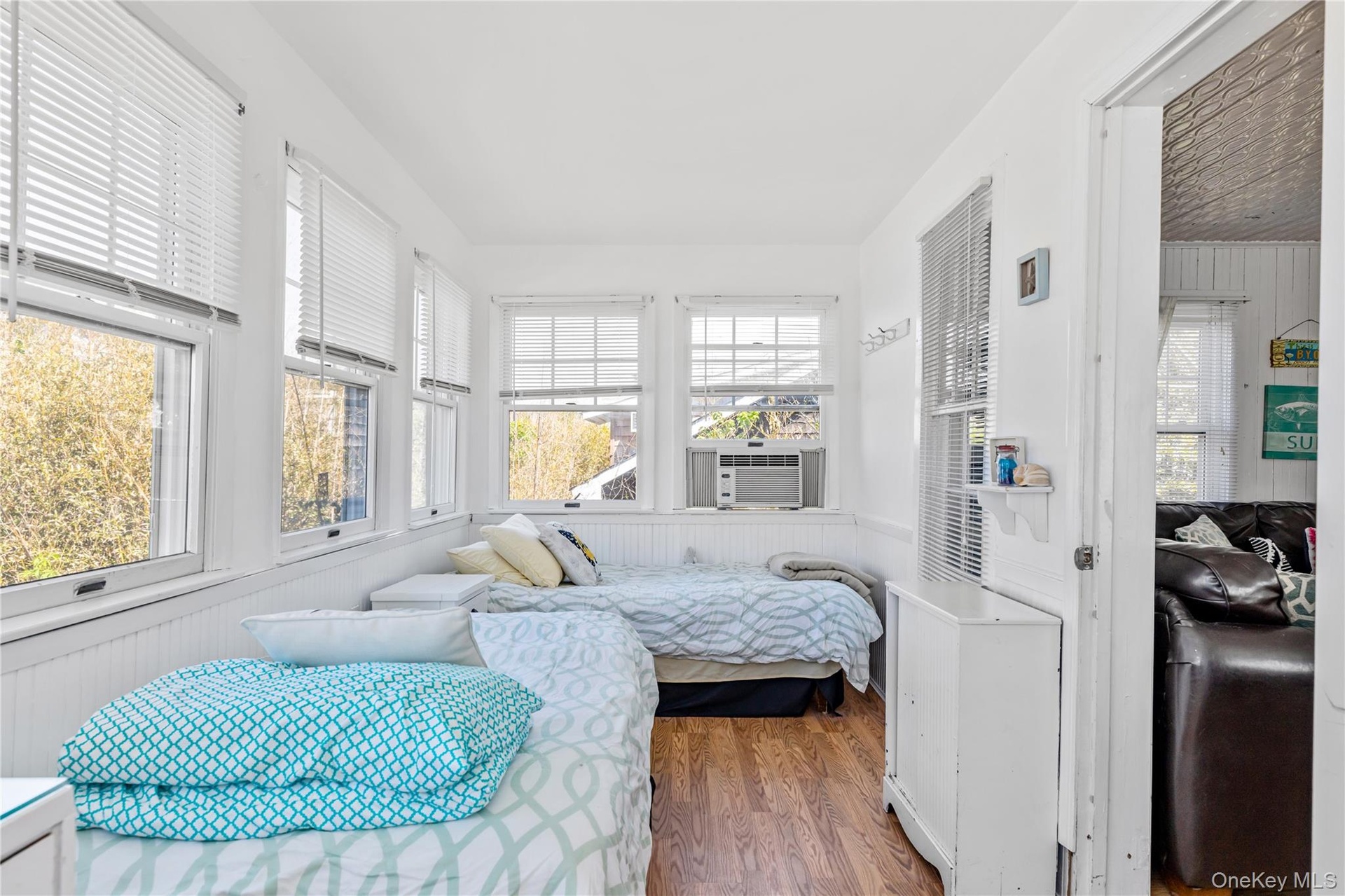 Sunroom featuring multiple windows with blinds, white wall paneling, wood-finish flooring, and an in-wall air conditioning unit