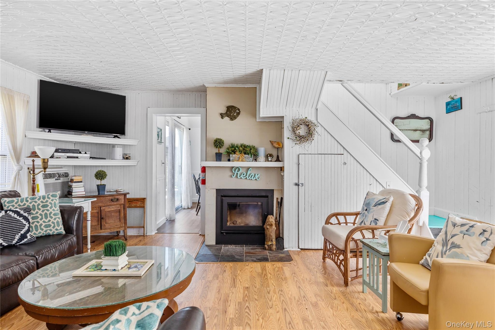 Living area featuring wood-finish flooring, a fireplace with a stone hearth, white shiplap walls, a white staircase with a paneled base, and a paneled