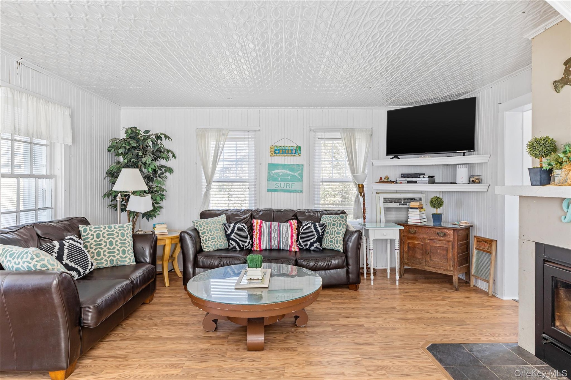 Spacious living area featuring wood-finish flooring, white beadboard walls, and a patterned ceiling