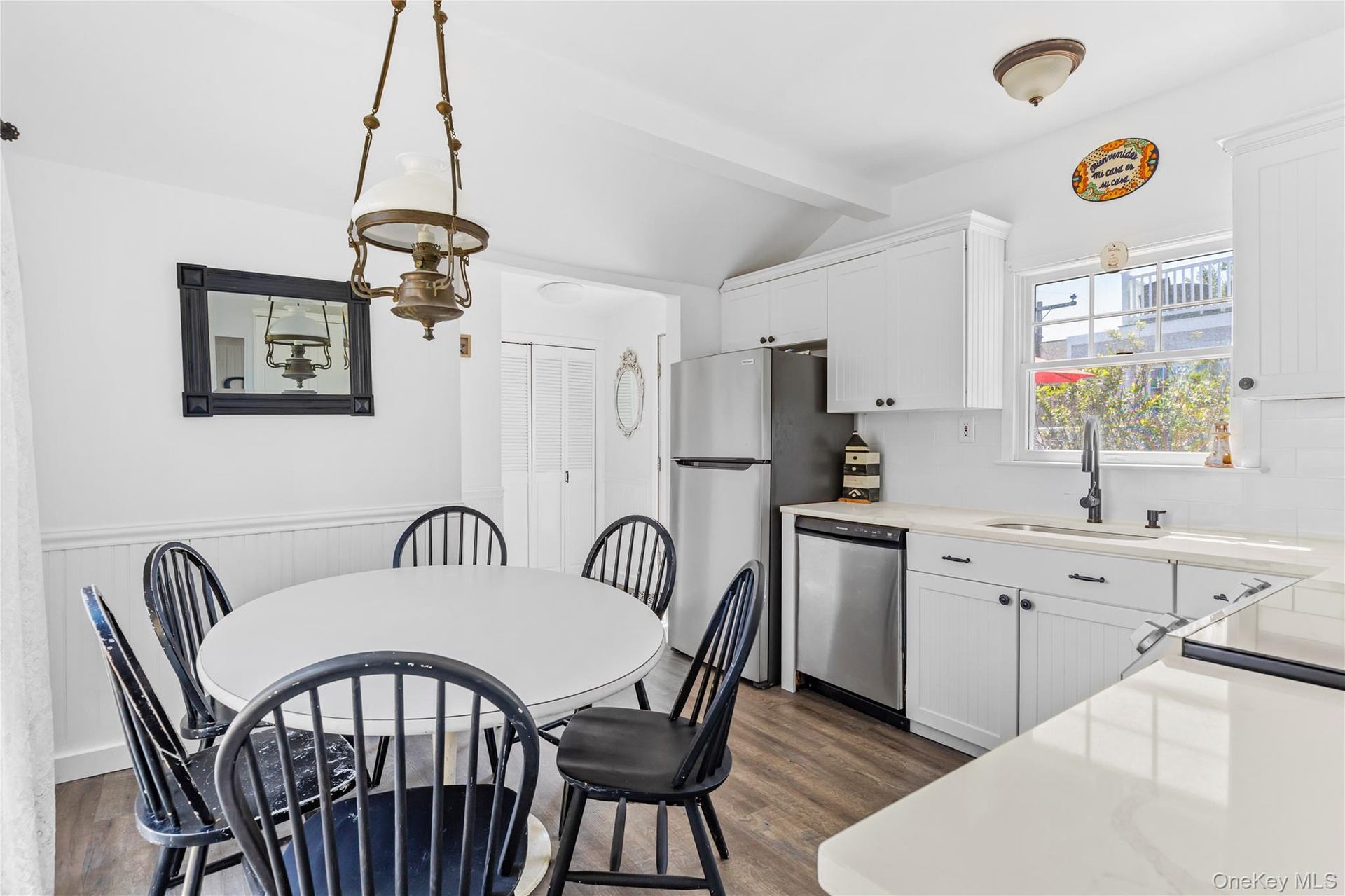 Bright kitchen and dining area featuring white cabinetry, light countertops, stainless steel appliances, and wood-finish flooring