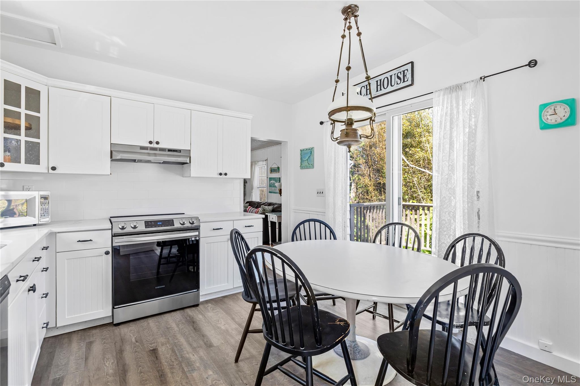 Kitchen and dining area featuring white cabinetry, a white subway tile backsplash, stainless steel range, and wood-finish flooring
