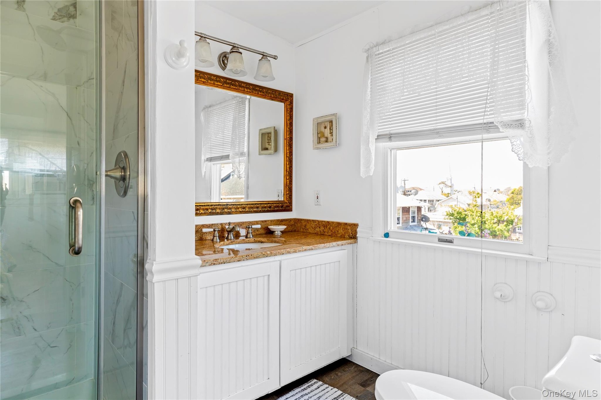 Bathroom featuring a glass-enclosed shower, single vanity with a granite countertop, and white beadboard paneling