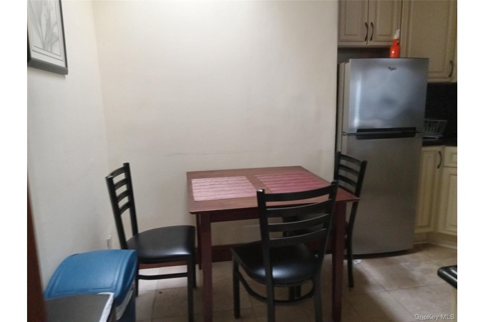 Compact dining area featuring a stainless steel refrigerator, light-toned cabinetry, and tiled flooring