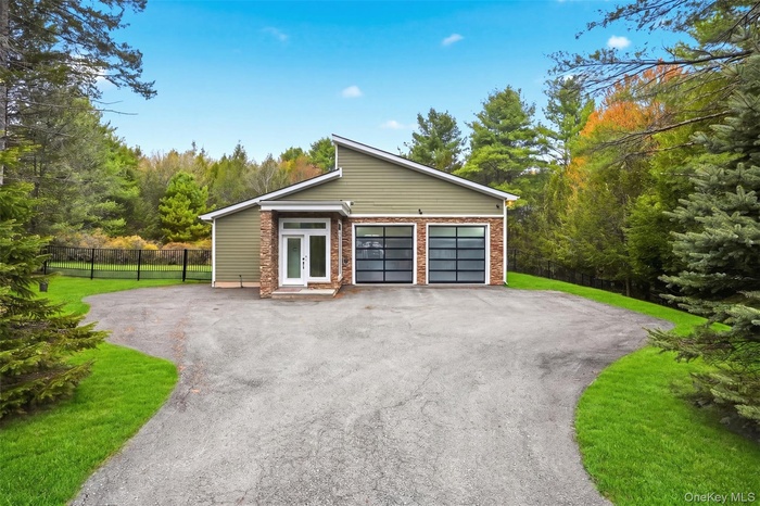 Modern ranch-style home featuring a four-car garage with frosted glass doors, a stone facade accent, and a light green exterior