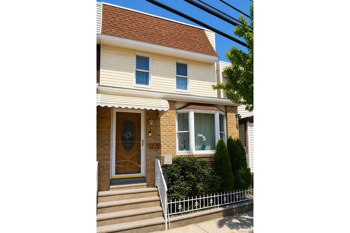 Two-story residence featuring a wood-finish entry door with decorative glass, a bay window, and a brown shingle roof