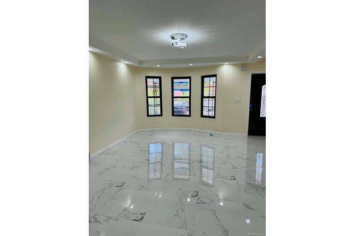 Spacious living area featuring large format marble-look tile flooring, bay windows with black muntins, a modern semi-flush mount ceiling fixture, rece