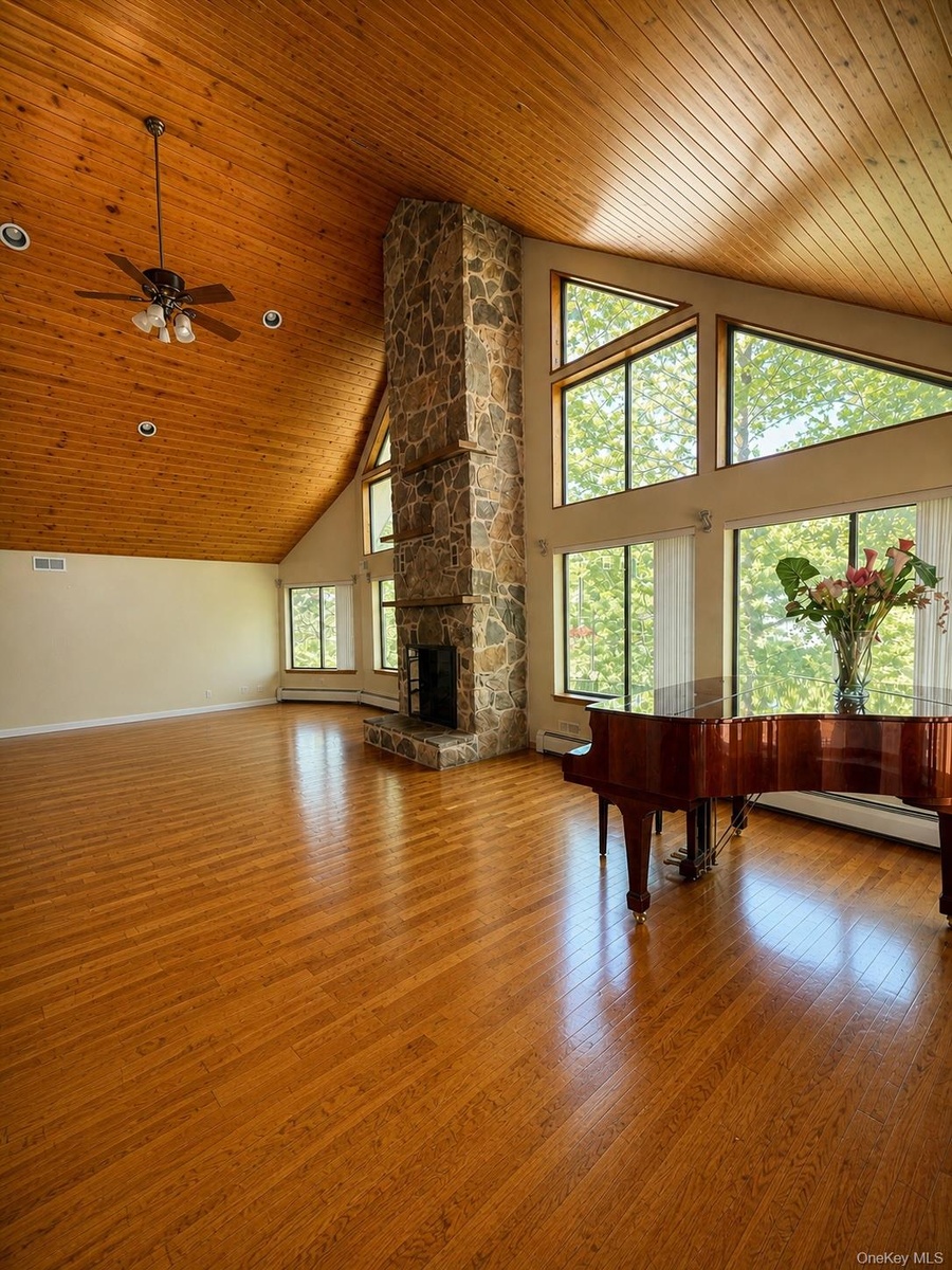 Spacious room featuring wood-finish flooring, a vaulted wood-paneled ceiling, a stone fireplace, large windows, and recessed lighting