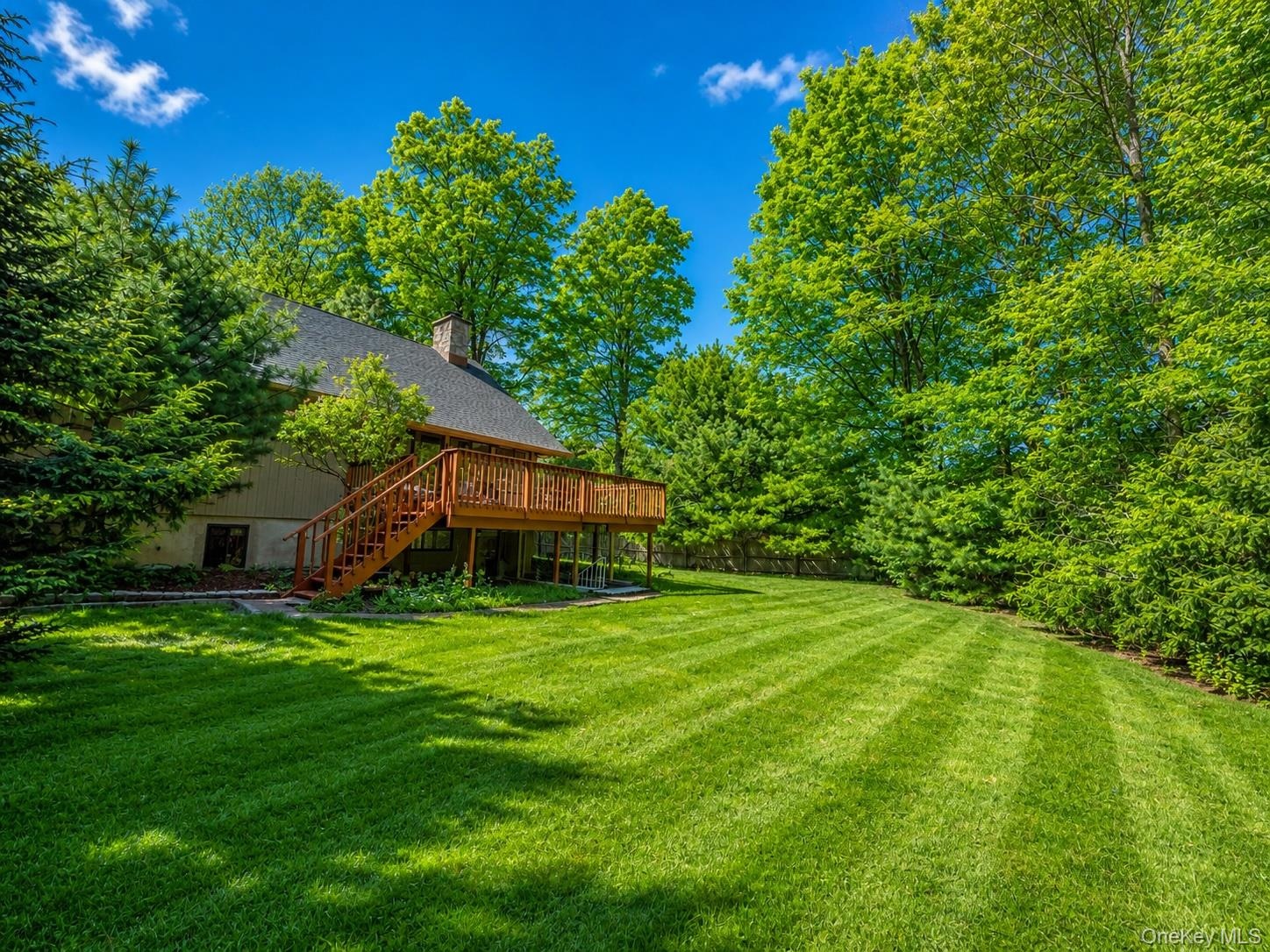 Expansive rear yard featuring a large wooden deck with staircase access