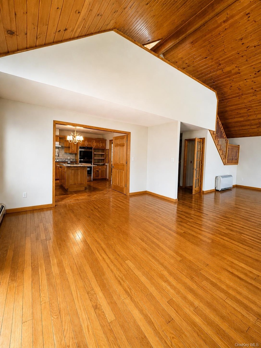 Spacious living area featuring high vaulted wood-paneled ceilings, polished wood-finish flooring, and white painted walls