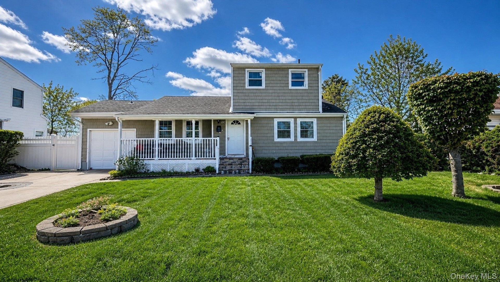 Residential property featuring a siding exterior, covered front porch with white railing, and a driveway leading to an attached garage