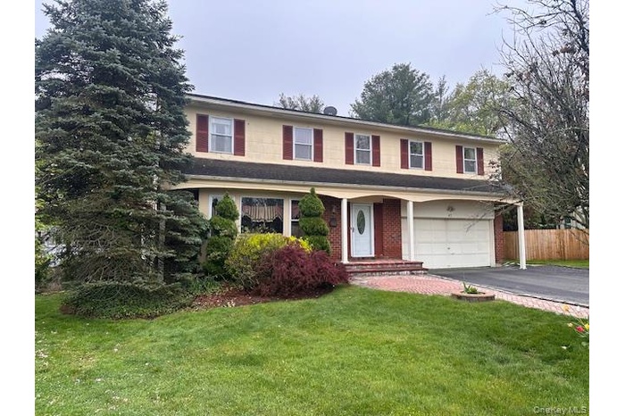 Traditional-style house with an attached garage, driveway, fence, and a front yard