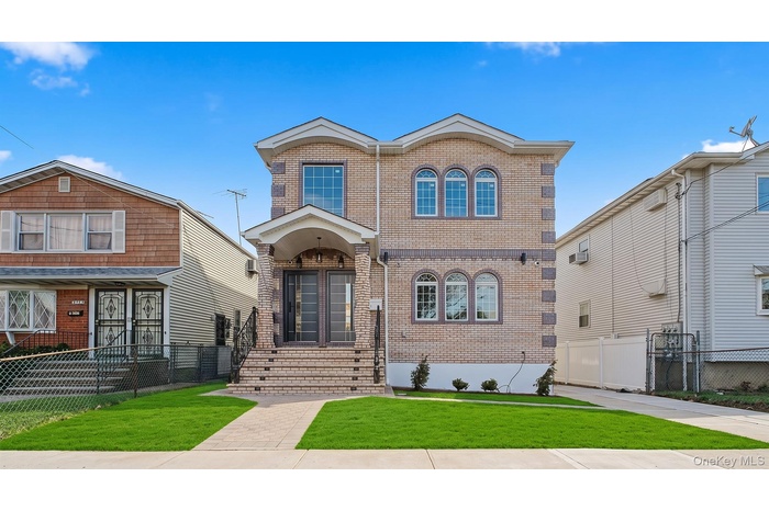 Contemporary brick facade residence featuring a covered entry porch, arched windows, dual entry doors, a paved driveway, and manicured front lawn