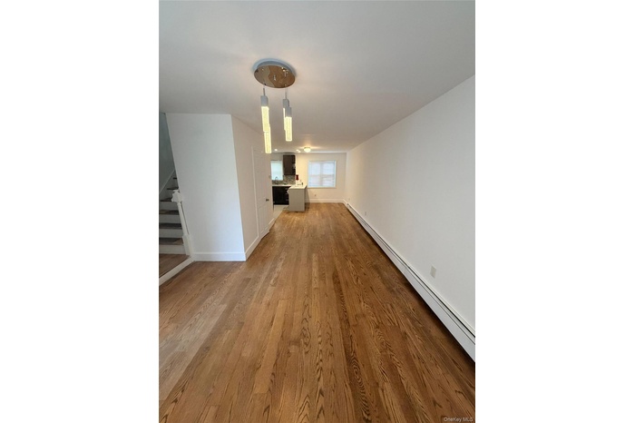 Spacious living area featuring wood-finish flooring, a modern multi-pendant light fixture, and white painted walls