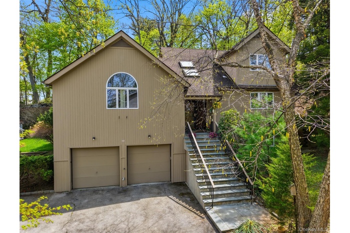 Split-level residence featuring a two-car garage with separate doors, an arched window accent, and a prominent exterior staircase with dark railings