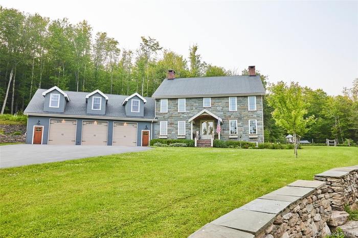 Colonial home with a front yard, a garage, a chimney, stone siding, and driveway