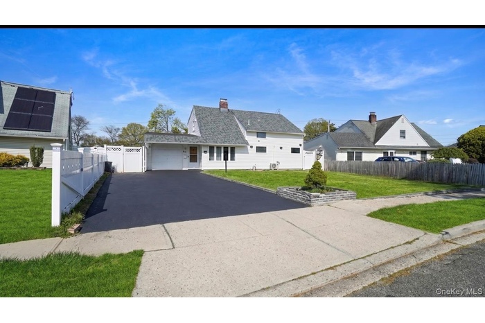 White-sided residence featuring a gray shingle roof, attached garage, paved driveway, and manicured front lawn