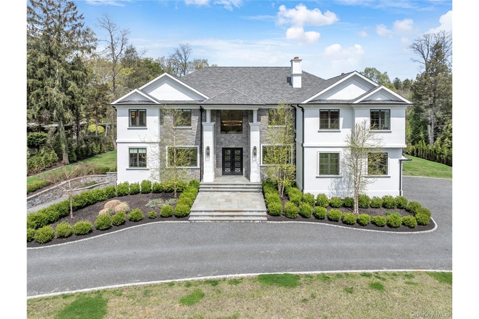 Stately residence featuring a stone and stucco exterior, prominent entryway with double doors, symmetrical window placement, and a multi-tiered roofli