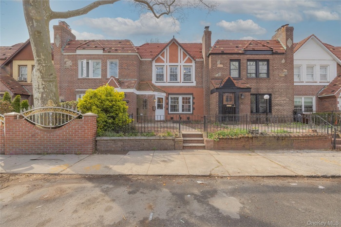 Charming brick facade featuring a gabled roofline, multiple white-framed windows, contrasting terracotta-colored stucco detailing, and a traditional f