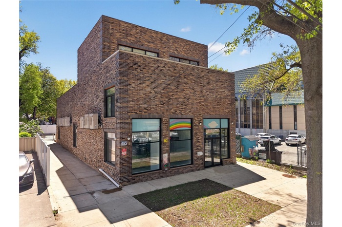Modern brick building featuring a multi-story facade, large storefront windows, and a paved sidewalk entrance
