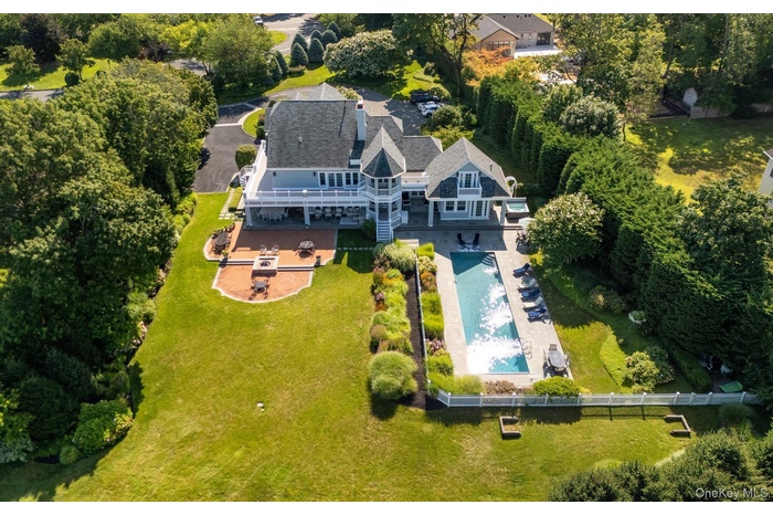 Expansive backyard featuring a rectangular swimming pool, a substantial paver patio with a built-in fire pit, and a spacious upper-level balcony
