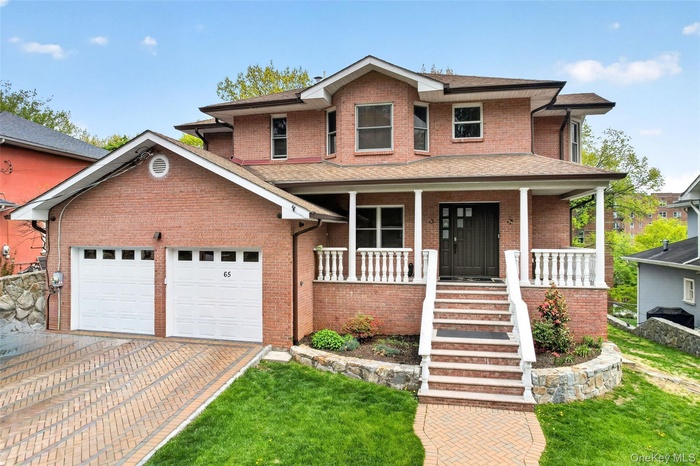 Brick exterior residence featuring a two-car garage, paved driveway, and covered front porch with white balustrades