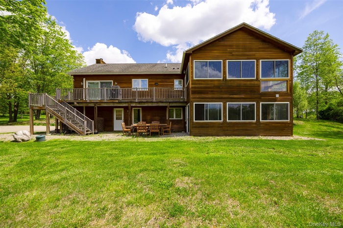 Rear view of property with a wooden deck, stairs, a yard, a chimney, and a patio area