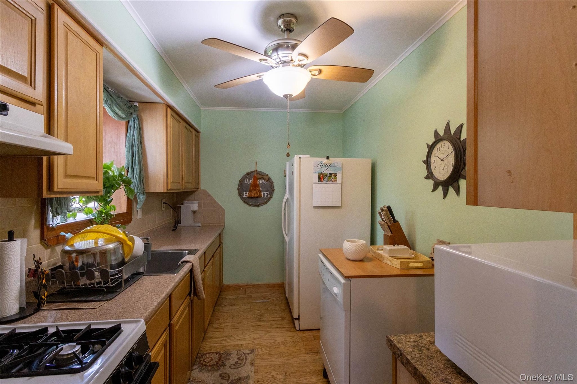 Galley kitchen featuring light wood-finish cabinetry, solid surface countertops, a stainless steel sink, and wood-finish flooring