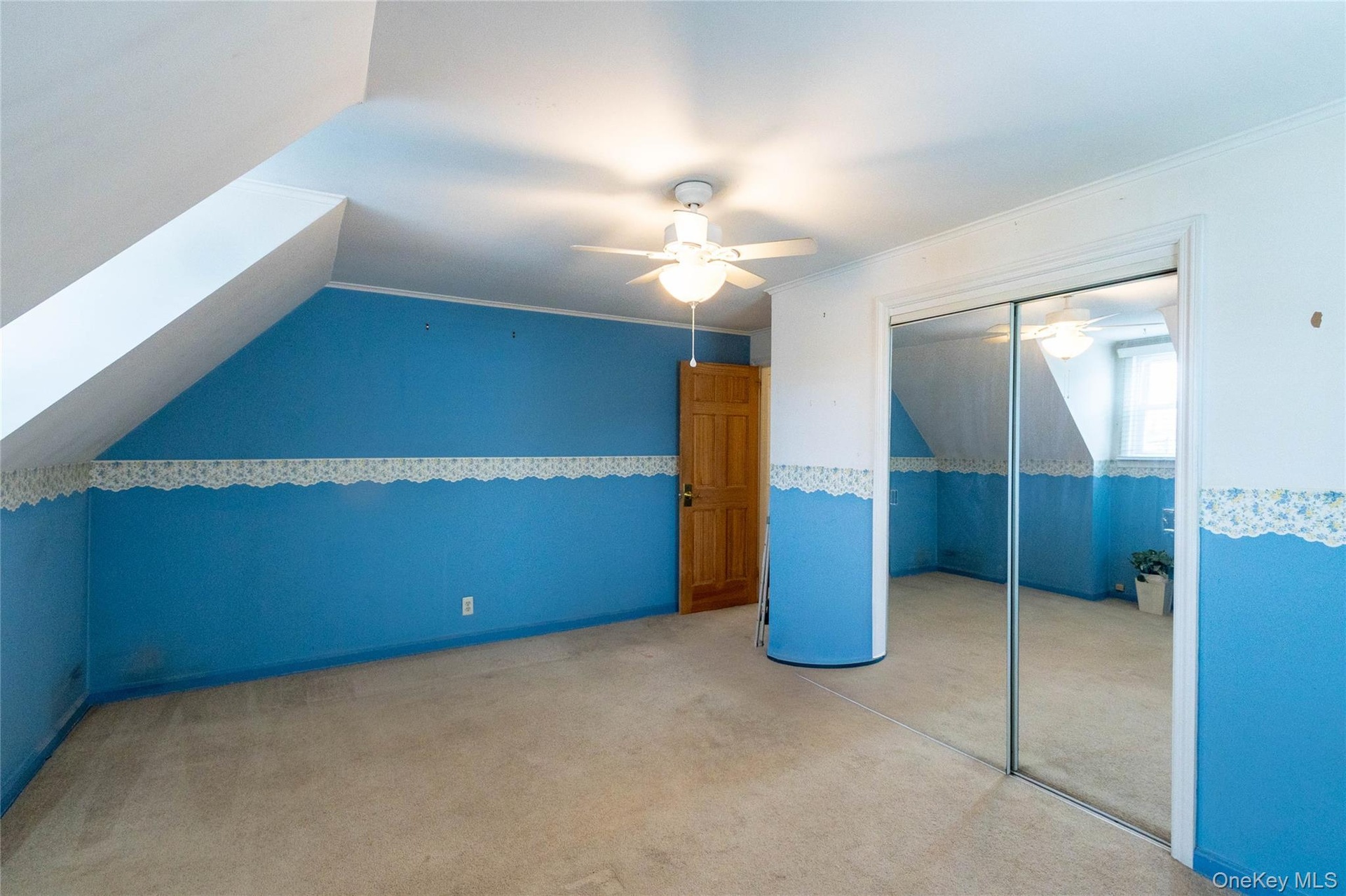 Attic room featuring sloped ceilings, a ceiling fan with light fixture, mirrored closet doors, and carpeted flooring