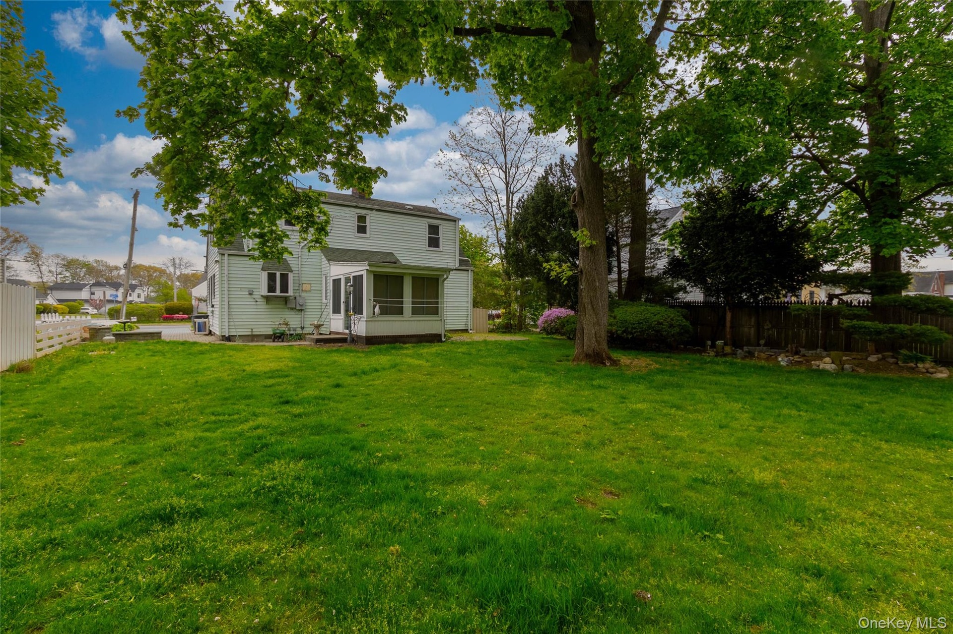 Expansive rear lawn featuring mature trees and a screened-in porch with a panel door
