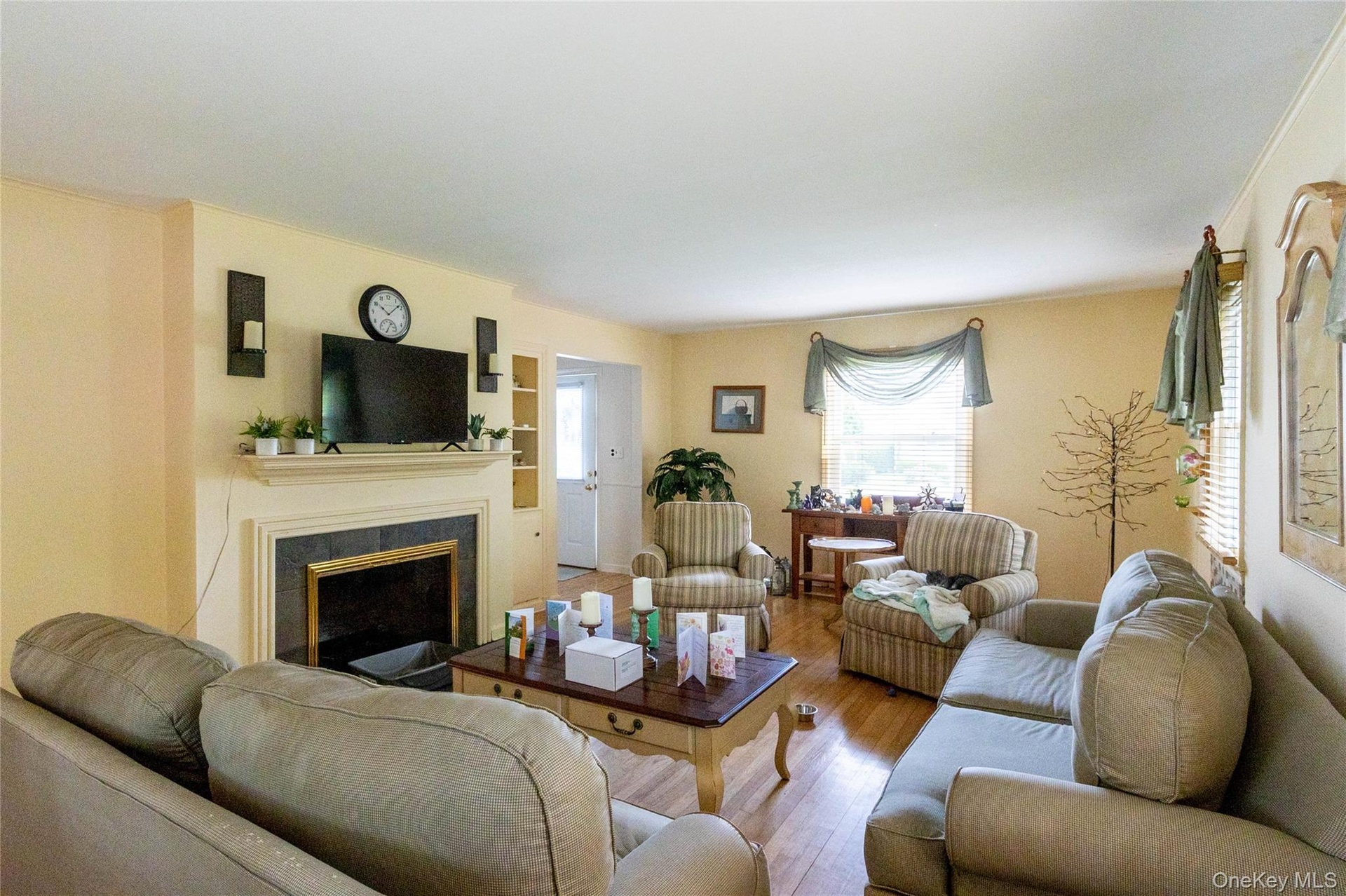 Spacious living area featuring warm-toned walls, wood-finish flooring, a fireplace with a black surround and white mantel, and built-in shelving