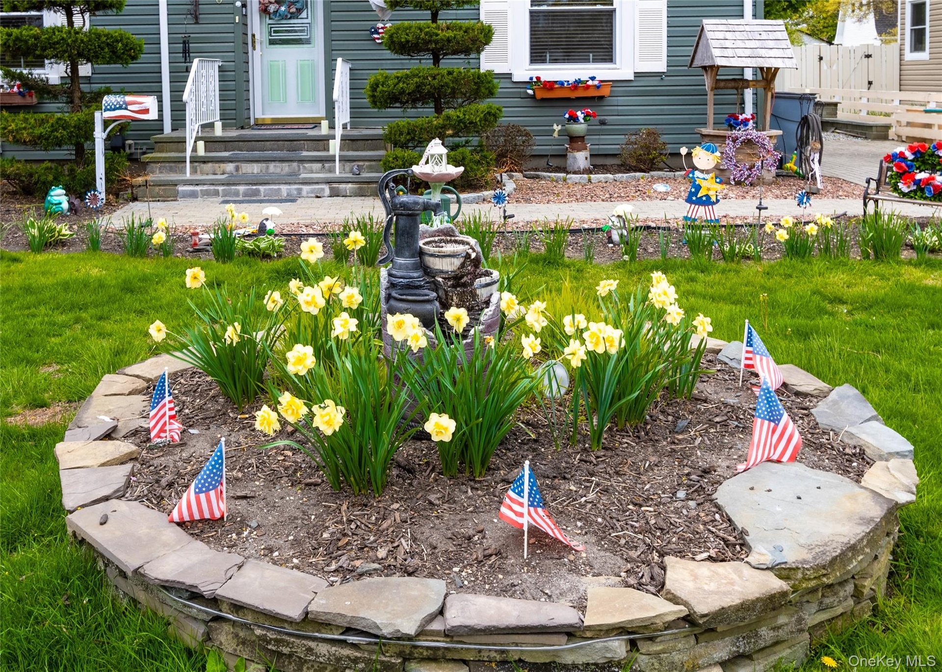 Front yard featuring a stone-lined flower bed with yellow blooms, a manicured lawn, and a paved walkway leading to the entrance
