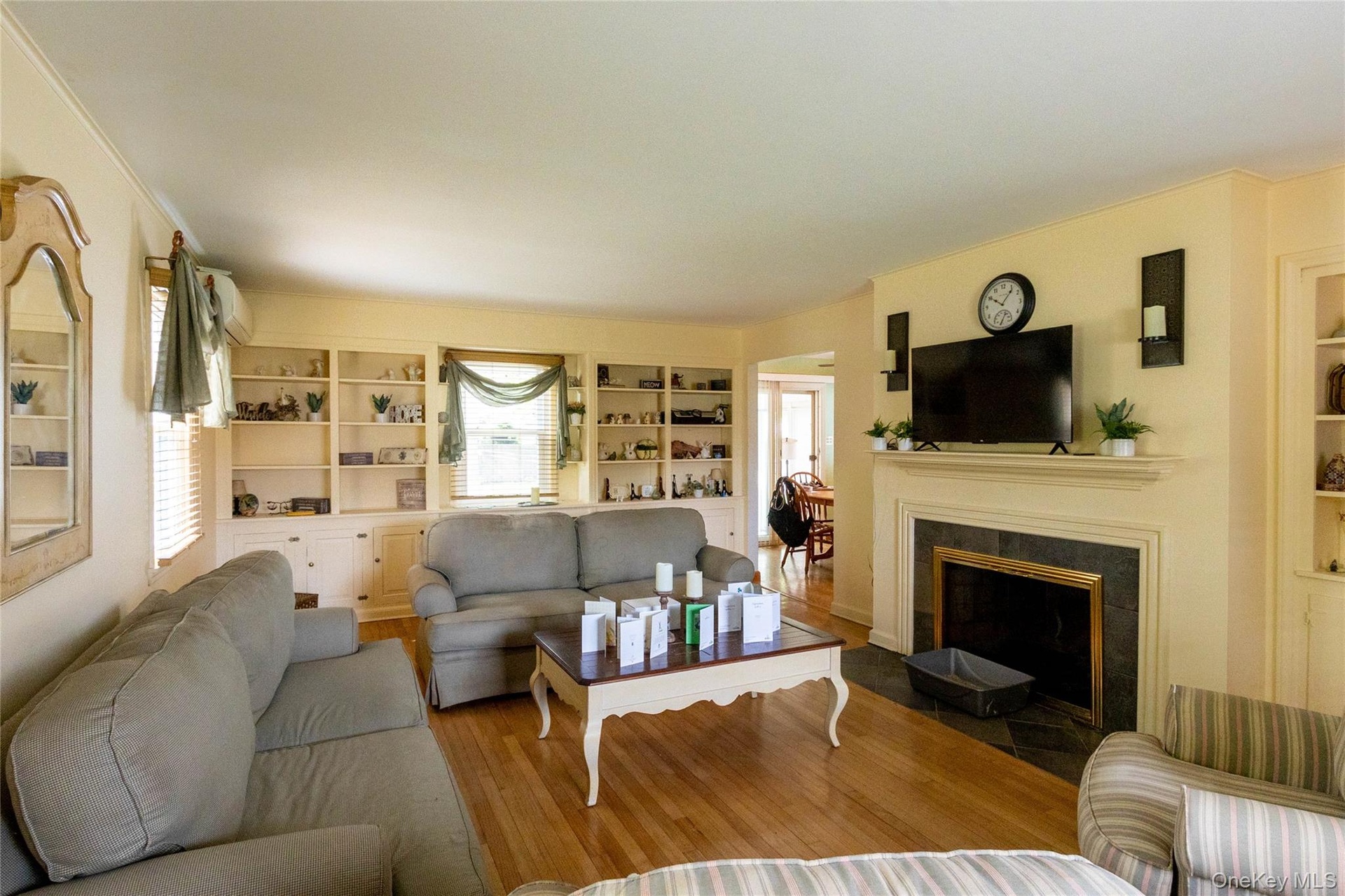 Living room featuring hardwood flooring, built-in shelving, a fireplace with a dark stone surround, and crown molding