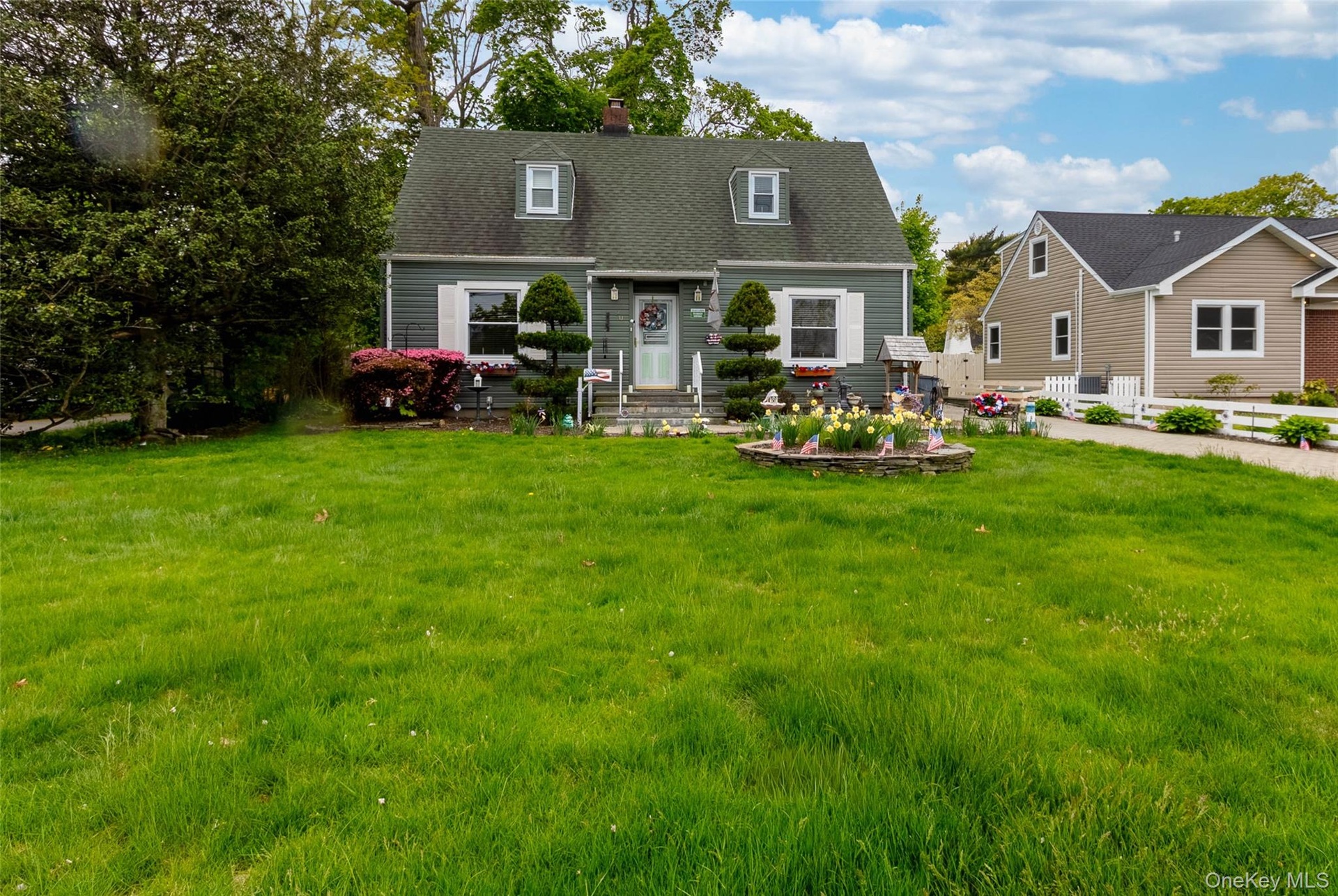 Gray siding exterior with white window shutters, a front entry door, and a dark shingle roof with two dormer windows