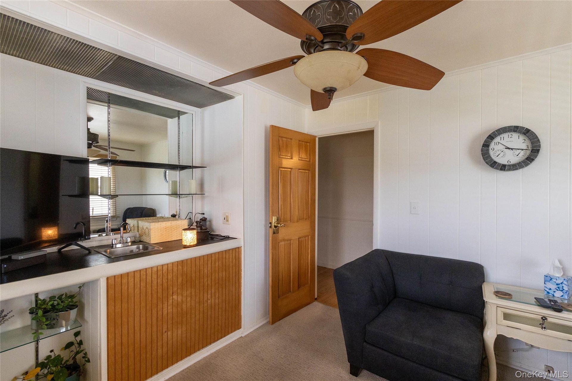 Integrated wet bar featuring a stainless steel sink, black countertop, mirrored backsplash, and glass shelving