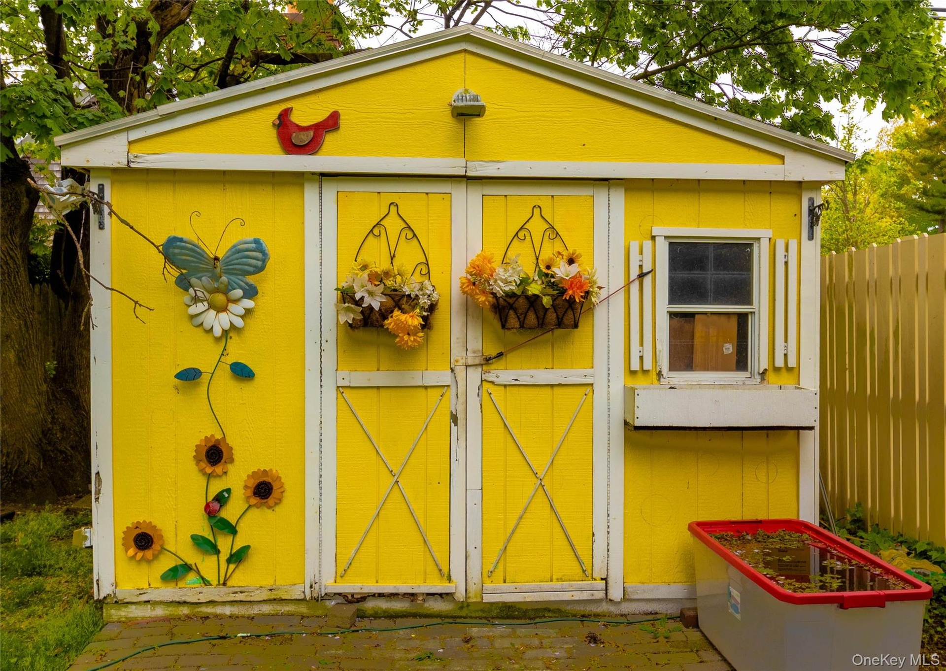 Bright yellow exterior shed with white trim, double entry doors, a side window with shutters, and an integrated window box