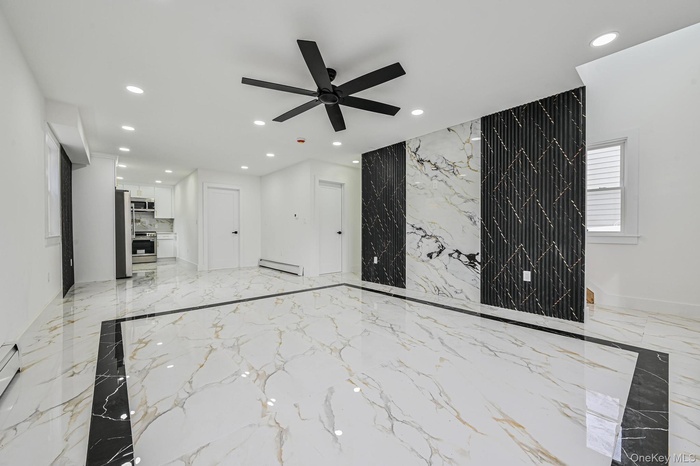 Open-concept interior featuring large format marble-look tile flooring with a black tile border, recessed ceiling lighting, a black ceiling fan, and a