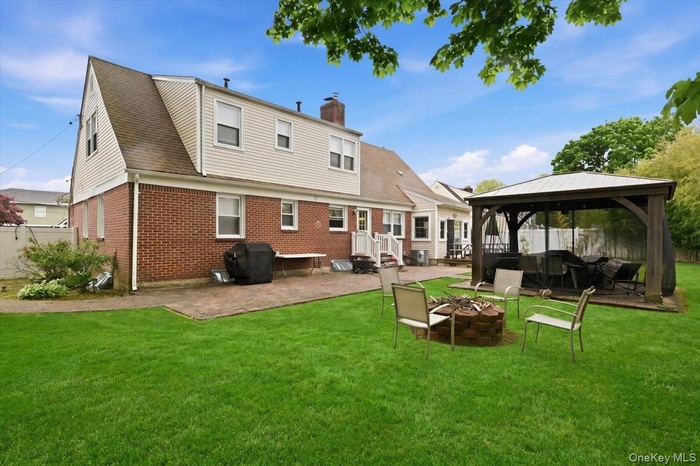 Beautiful view of the Expansion to this Rear Cape featuring a lush lawn, brick paver patio, and a built-in fire pit