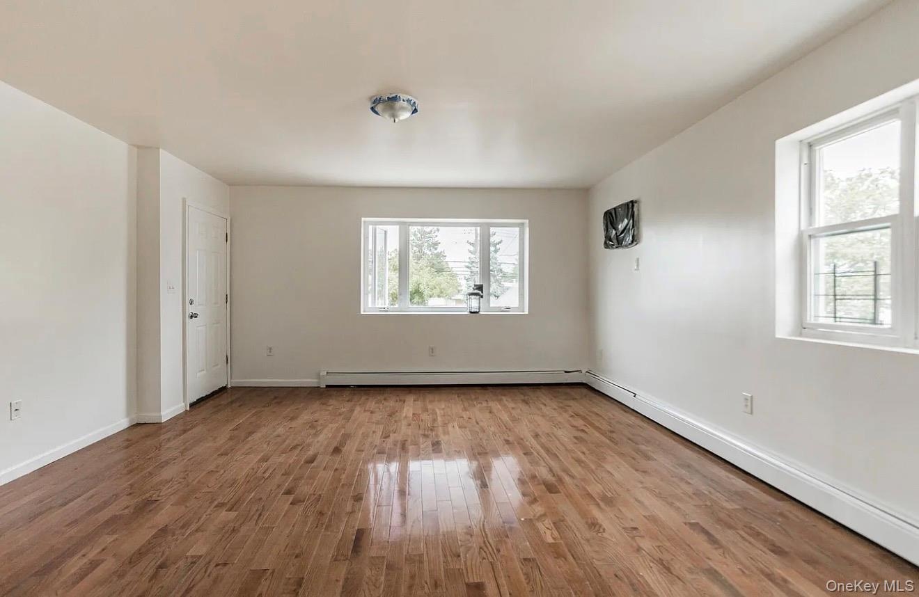 Spacious room featuring wood-finish flooring, white walls, and multiple windows