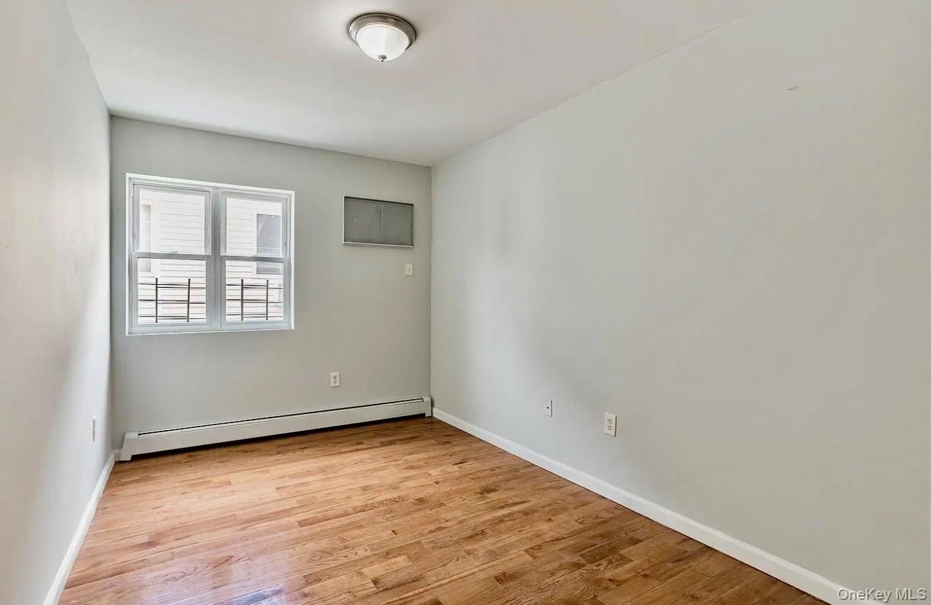 Room featuring wood-finish flooring, a double-hung window, white baseboards, and a semi-flush ceiling light fixture