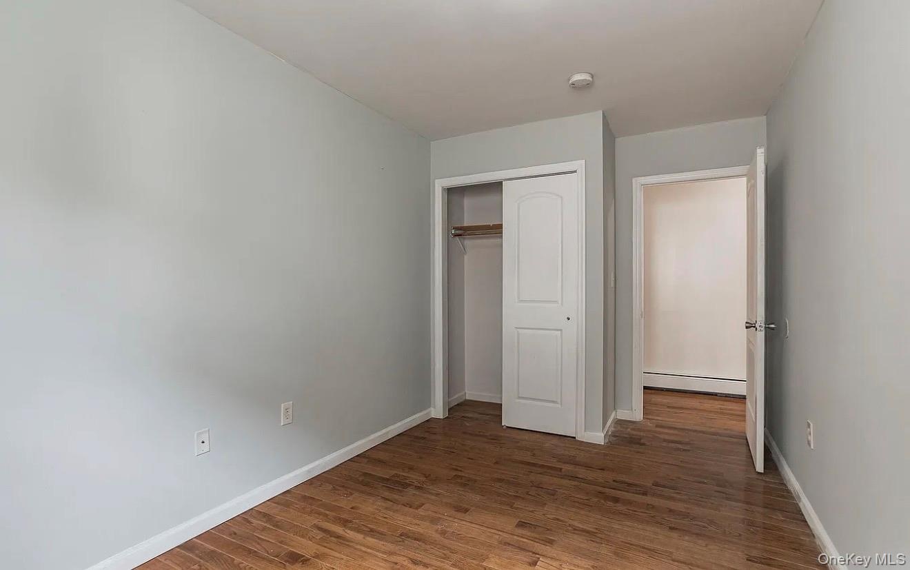 Room featuring wood-finish flooring, light gray walls, white trim, and a built-in closet with white bifold doors