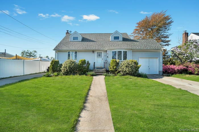 Light blue siding residence featuring a front lawn with a concrete walkway, a white privacy fence, a driveway, and an attached garage