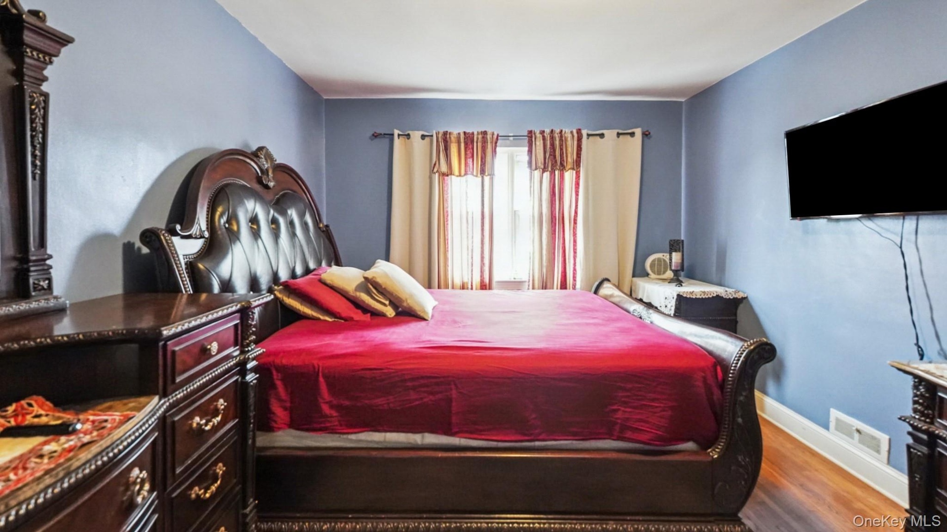 Bedroom featuring wood-finish flooring, a wall-mounted television, and baseboard registers