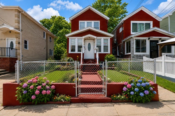 Red-sided residence featuring a front porch w white railing, a terraced front lawn, and a chain-link fence. digitally enhanced