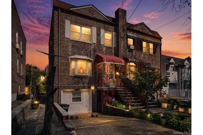 Brick facade residence featuring a prominent bay window with white shutters, a red alluminum awning, and a stone-lined planter bed